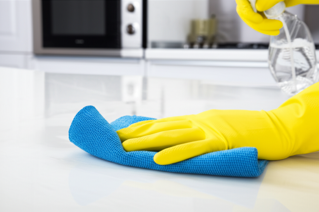 Hands in rubber gloves wiping kitchen benchtop for hygiene and pest prevention
